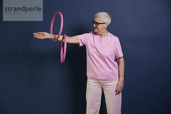 Ältere Frau übt mit Reifen vor blauem Hintergrund