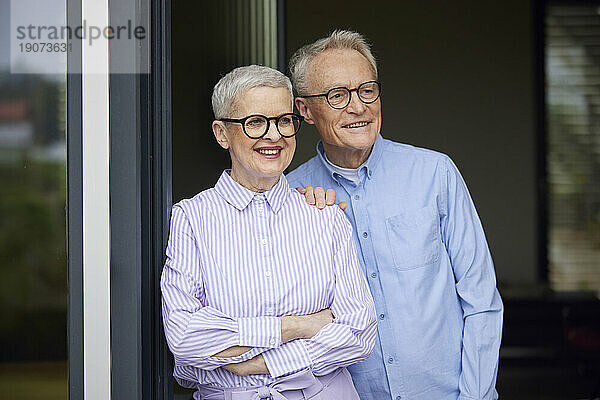 Happy senior couple standing at balcony door