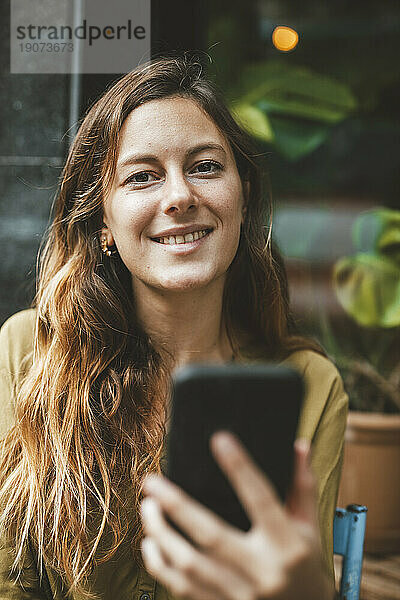 Lächelnde junge Frau mit Smartphone im Café