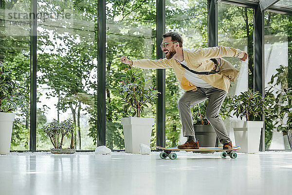 Fröhlicher Geschäftsmann beim Longboard-Skaten vor dem Fenster