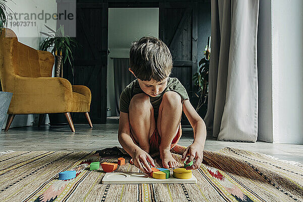 Junge spielt mit Bauklötzen und kauert zu Hause auf dem Teppich