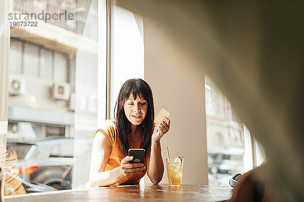 Lächelnde reife Frau benutzt Smartphone am Tisch im Café