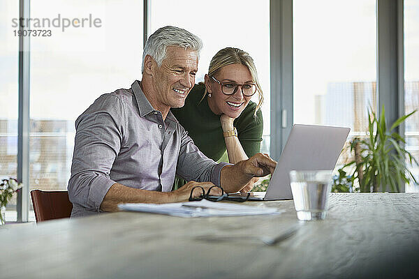 Lächelndes älteres Paar  das zu Hause einen Laptop auf dem Tisch benutzt