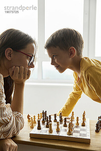 Lächelnder Junge  der zu Hause mit seiner Mutter Schach spielt