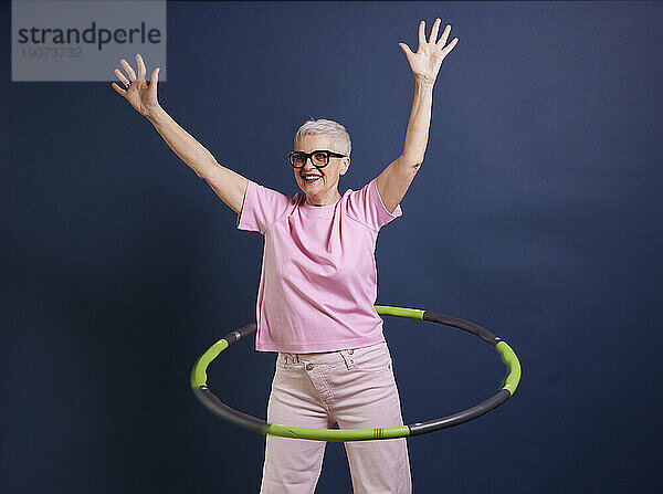 Ältere Frau übt Hula-Hoop vor blauem Hintergrund