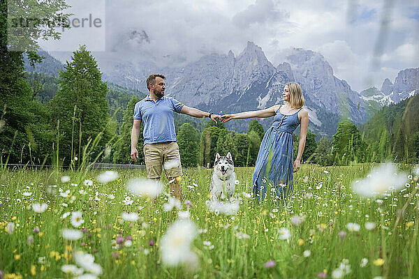 Man and woman holding hands with Husky dog in front of mountains