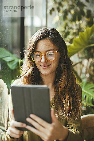 Lächelnde Frau mit Brille und Tablet-PC im Café