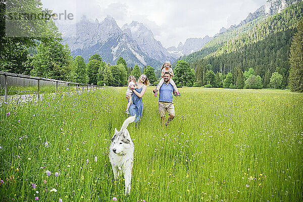 Familie verbringt Urlaub mit Hund beim Gassigehen auf Gras vor Bergen