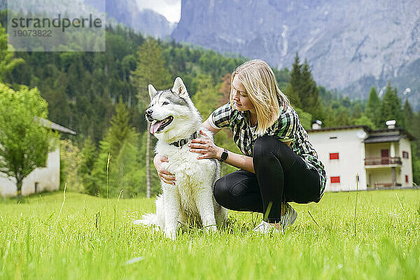 Frau kauert neben Hund im Gras