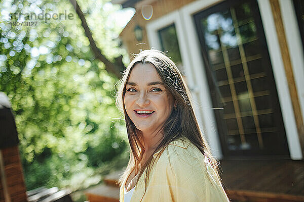Lächelnde Frau auf der Veranda vor dem Haus