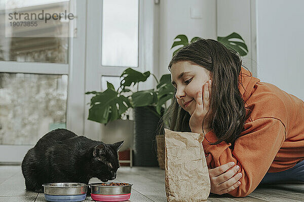 Lächelndes Mädchen beobachtet Katze beim Fressen zu Hause