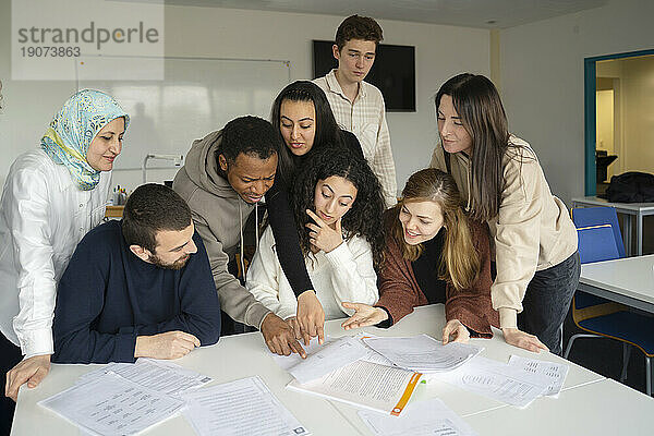 Schüler zeigen auf Papiere  die im Klassenzimmer auf dem Tisch liegen