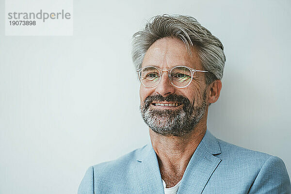 Lächelnder Geschäftsmann mit Brille vor weißer Wand