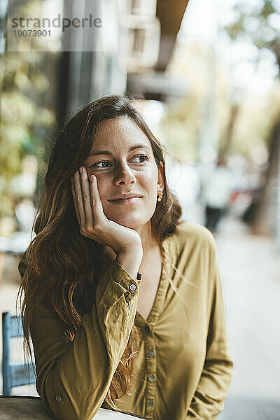 Nachdenkliche Frau sitzt mit der Hand am Kinn im Café