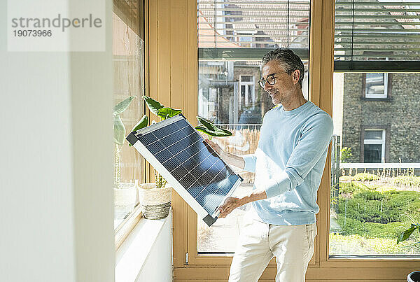 Lächelnder Geschäftsmann untersucht Solarpanel im Büro