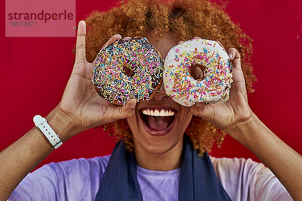 Verspielte Frau hält zwei Donuts vor ihren Augen