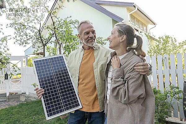 Glückliches Paar mit Solarpanel vor dem Haus