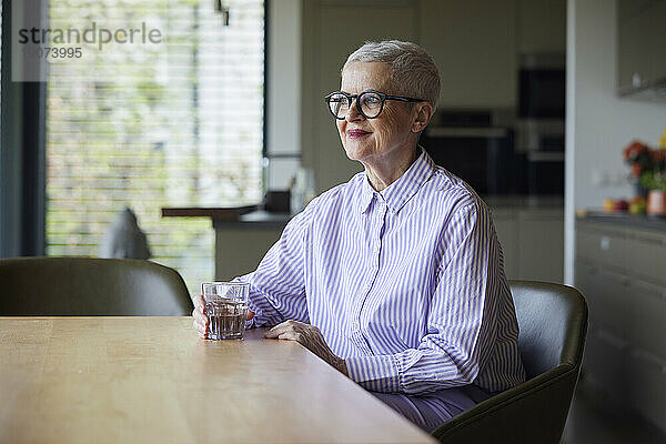 Selbstbewusste ältere Frau sitzt zu Hause am Tisch