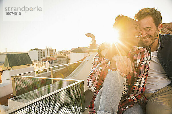 Happy affectionate young couple sitting on rooftop at sunset