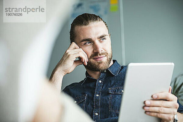 Portrait of businessman with tablet in office thinking