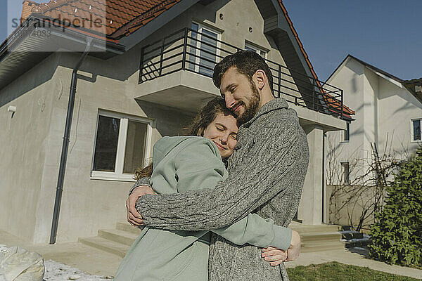 Lächelndes Paar  das sich vor dem neuen Haus umarmt