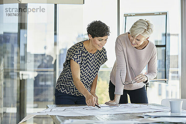 Two smiling businesswomen discussing plan on desk in office