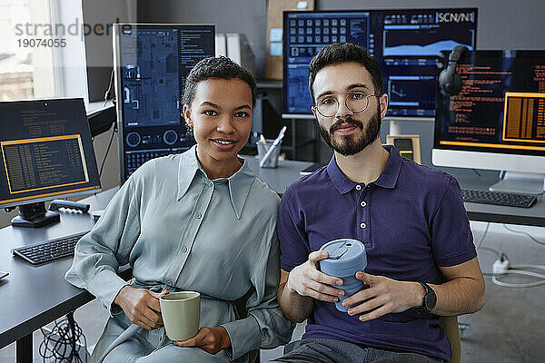 Lächelnde IT-Experten sitzen zusammen mit Kaffeetassen im Büro