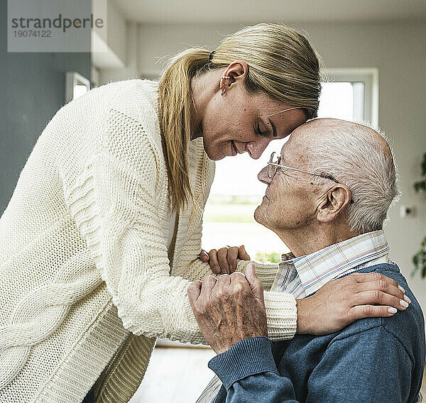 Lächelnde blonde Frau kümmert sich zu Hause um den Vater und umarmt ihn