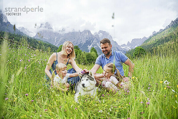 Familie genießt Urlaub mit Hund  der im Gras vor den Bergen sitzt