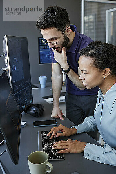 Junger Computerprogrammierer mit Kollege  der am Schreibtisch auf der Tastatur tippt