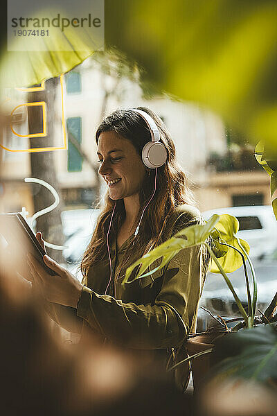 Glückliche Frau trägt Kopfhörer  hört Musik und benutzt Tablet-PC im Café