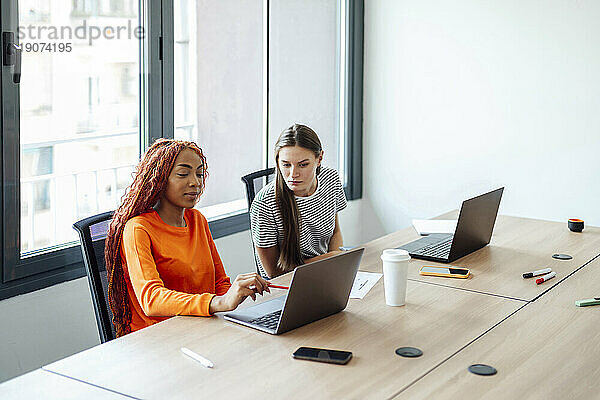 Lächelnde Geschäftsfrau diskutiert mit Kollegen am Laptop