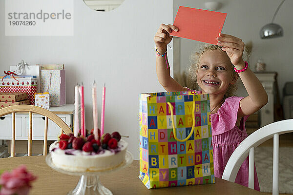 Lächelndes Mädchen hält Geburtstagskarte zu Hause