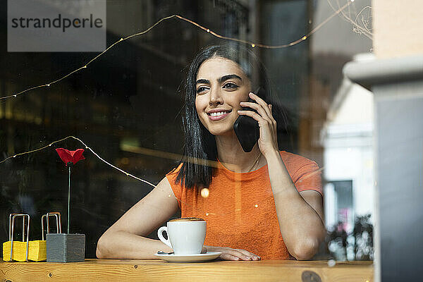 Lächelnde junge Frau  die im Café sitzt und mit ihrem Smartphone spricht