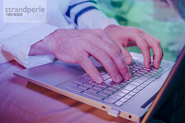 Hände eines Mannes  der einen Laptop im Neonlicht benutzt