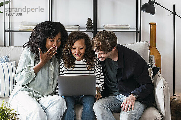 Eltern sitzen auf dem Sofa und surfen mit ihrer Tochter am Laptop im Internet