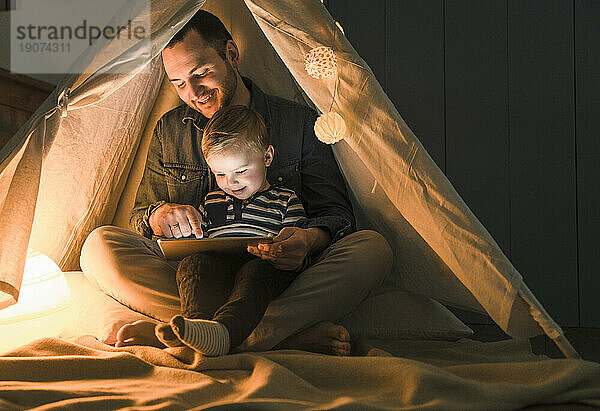 Vater und Sohn teilen sich ein Tablet in einem dunklen Zelt zu Hause