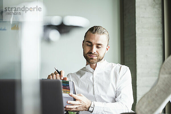 Junger Geschäftsmann sitzt mit erhobenen Füßen im Büro und benutzt ein Tablet