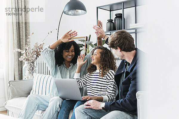 Glückliche Eltern sitzen mit ihrer Tochter auf dem Sofa und benutzen Laptop