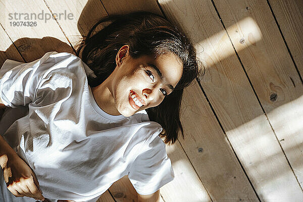 Lächelnde junge Frau  die zu Hause auf dem Hartholzboden liegt