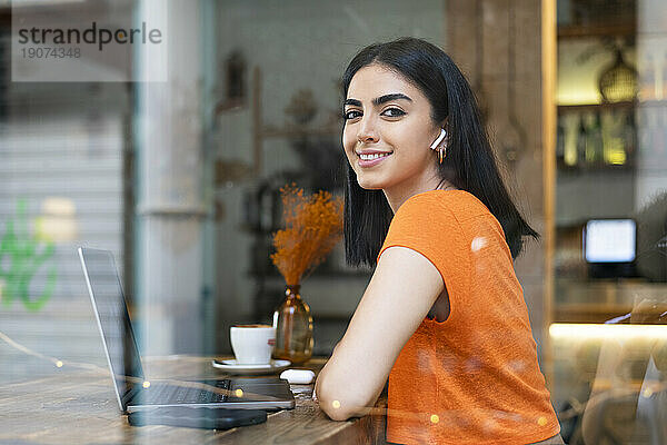 Lächelnde junge Geschäftsfrau mit Laptop sitzt im Café