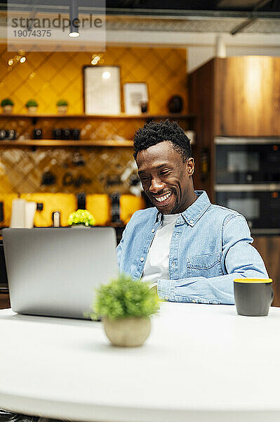 Lächelnder Geschäftsmann mit Laptop auf dem Tisch im Büro