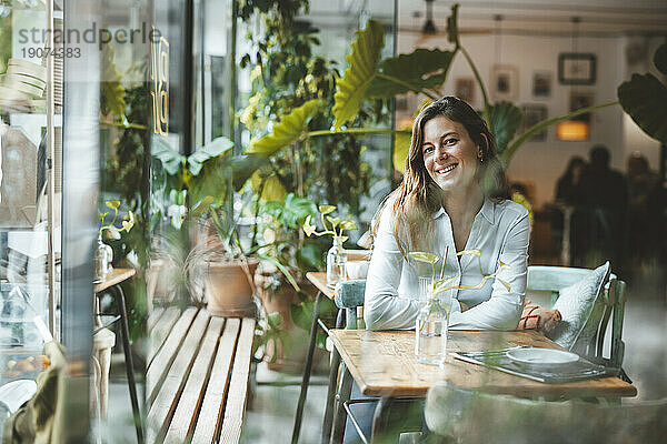 Glückliche junge Frau sitzt am Tisch im Café