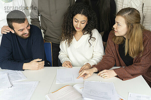 Frau hilft Freunden beim Lernen mit Notizen auf dem Tisch im Klassenzimmer