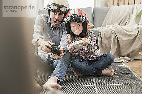 Junger Mann und kleines Mädchen tragen Bikerhelme und spielen Rennspiel mit Spielekonsolen
