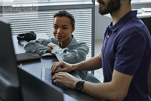 Lächelnder IT-Experte mit Kollege  der im Büro am Computer arbeitet