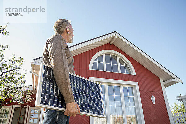 Mann blickt auf Haus mit Solarpanel