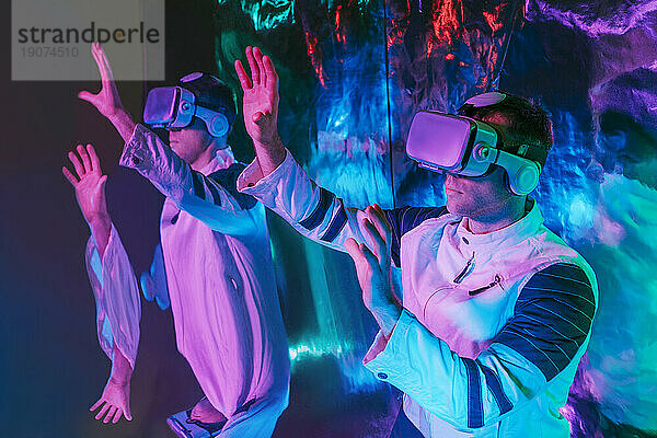 Mann trägt einen Virtual-Reality-Simulator und gestikuliert vor einem Spiegel im Neonlicht