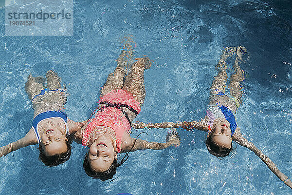 Carefree friends with arms outstretched swimming in pool