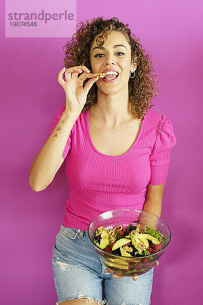 Glückliche Frau isst Salat vor magentafarbenem Hintergrund
